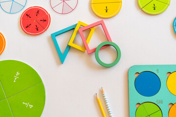 Colorful educational math manipulatives arranged on a table with circular fraction pieces and geometric shapes indicating a learning environment for children