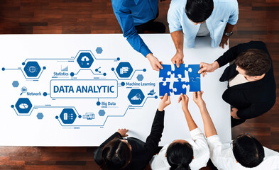 A diverse group of professionals collaborates on data analytic strategies, using puzzle pieces symbolizing teamwork and innovative technology in a modern workspace. Amity