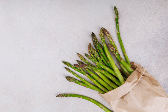 Bundle of fresh green asparagus in brown paper wrap on light ceramic surface, top view