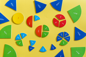 Colorful educational fraction manipulatives arranged on a bright yellow surface for hands-on learning activities in a classroom setting