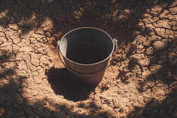 "Arid Scene: An empty metal bucket sits forlornly in the cracked earth, a poignant symbol of drought and environmental challenge. It represents the scarcity and the stark reality. 