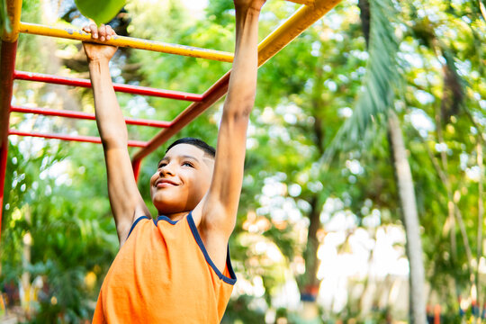 Young boy having fun exercising outdoors hanging from monkey bars in a park