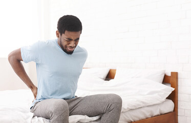 Bad bed. Young african-american guy suffering from back pain in bedroom, waking up in morning, free...