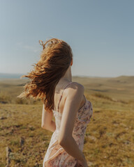 Girl in summer dress on mountain looking into the distance. Wind blowing hair
