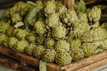 Fresh green artichokes with green leaves displayed on a counter in a street food market, close up