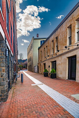 Red brick sidewalk between the walls of houses under a blue sky with clouds.