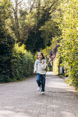 Fototapeta premium Joyful child running along a sunlit pathway surrounded by lush greenery and vibrant foliage, embodying carefree childhood moments and happiness