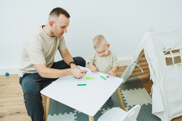Dad teaches his 1.6 year old son to sculpt from plasticine. The toddler boy sits at the children's...