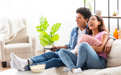 Obraz premium Watching Comedy Film. Loving Teenage Couple Resting On Sofa And Laughing, Empty Space