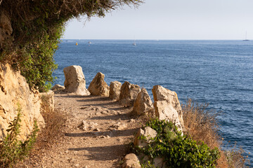 Rocky pathway winding along the beautiful coastline of Saint-Jean-Cap-Ferrat, France, with the azure sea and boats in the background.