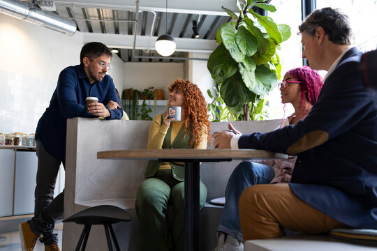 Coworkers chatting and drinking coffee during break in modern office