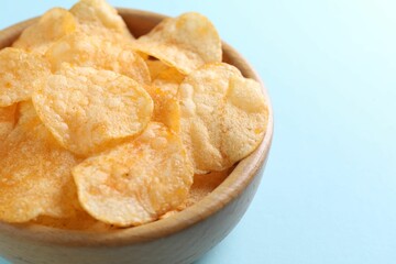 Tasty potato chips in bowl on light blue background, closeup. Space for text