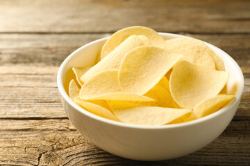 Tasty potato chips in bowl on wooden table, closeup