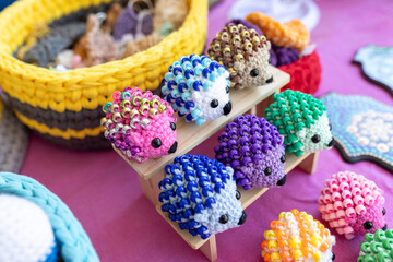 A colorful collection of Fidget Hedgehogs, small crocheted toys with beaded quills, are displayed on a miniature wooden stand at a market
