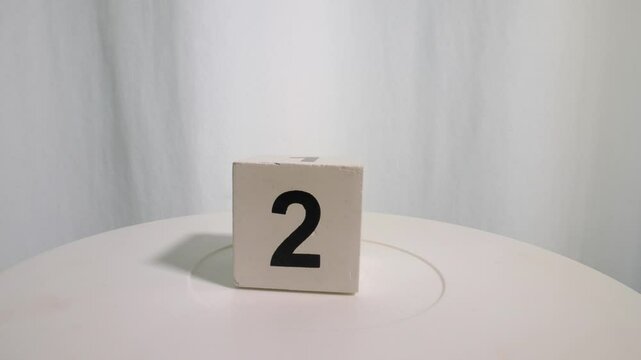 Wooden cube with the number 2 on a turntable on a white background. Slow motion