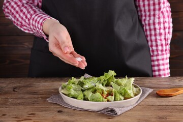 Woman salting tasty salad at wooden table, closeup