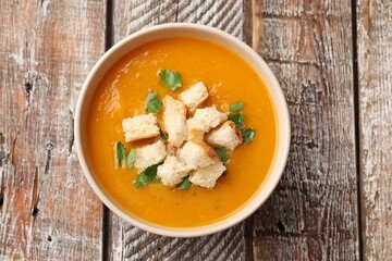Tasty pumpkin cream soup with croutons and parsley in bowl on wooden table, top view