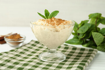 Delicious rice pudding with cinnamon and mint in glass dessert bowl on white table, closeup