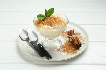 Delicious rice pudding with cinnamon, mint and spoons on white wooden table