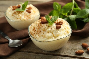 Delicious rice pudding with cinnamon, almonds and mint served on wooden table, closeup