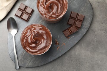 Tasty pudding and pieces of chocolate on grey table, flat lay