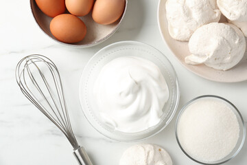 Delicious homemade meringue cookies, ingredients and whisk on white marble table, flat lay