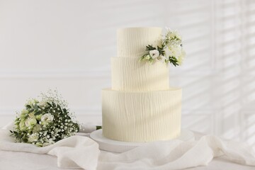 Delicious wedding cake with floral decor and bouquet on table indoors