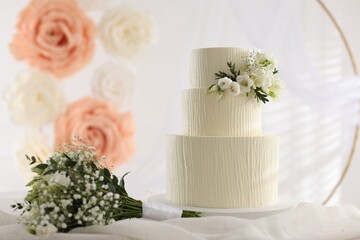 Delicious wedding cake with floral decor and bouquet on table indoors