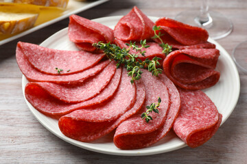 Slices of delicious sausage with thyme served on light wooden table, closeup
