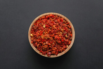 Red chili pepper flakes in bowl on dark table, top view