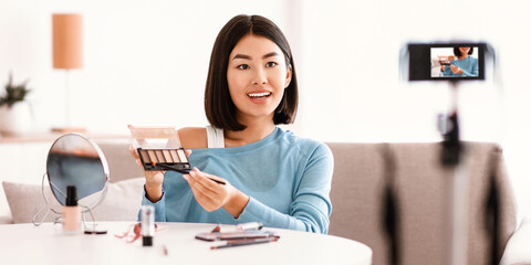 Blogging Concept. Young asian vlogger sitting next to camera, recording video for her internet channel in social media. Lady shooting beauty blog about cosmetics and makeup, showing her shadow palette