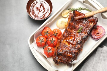 Delicious spare ribs, rosemary, baked onion, sauce and sun dried tomatoes on grey table, flat lay. Space for text