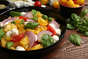 Tasty salad with yellow tomatoes, basil, onion and mozzarella cheese on wooden table, closeup