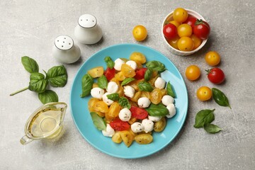 Tasty salad with yellow tomatoes, basil and mozzarella cheese on light grey table, flat lay