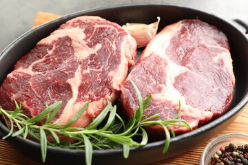 Pieces of raw beef meat and spices in baking dish on table, closeup