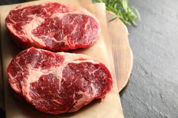 Pieces of raw beef meat and rosemary on black table, closeup. Space for text
