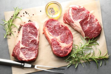 Pieces of raw beef meat, spices and carving fork on grey table, flat lay