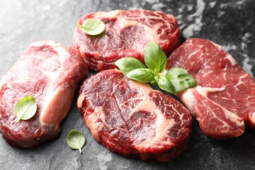 Pieces of raw beef meat and basil on dark table, closeup