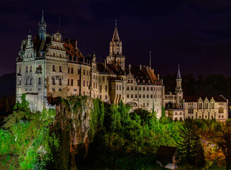 Fototapeta premium Illuminated castle at night surrounded by lush greenery creates a fairytale atmosphere in the countryside