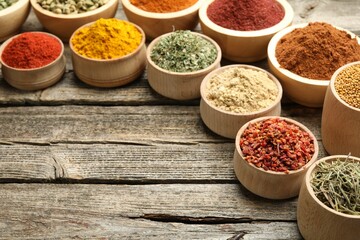 Different aromatic spices in bowls on wooden table, closeup. Space for text