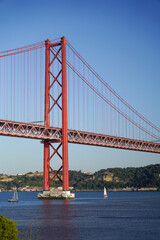 Fototapeta premium Majestic Red Suspension Bridge over Water with Sailboats Lisbon Portugal The Ponte 25 de Abril suspension bridge