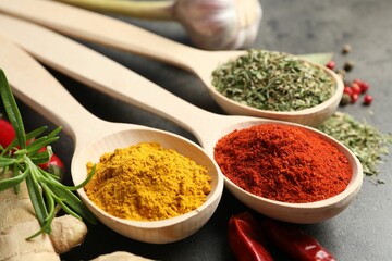 Many different spices in spoons on grey table, closeup