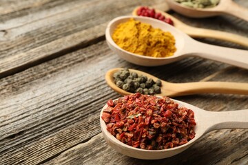 Different aromatic spices in spoons on wooden table, closeup. Space for text