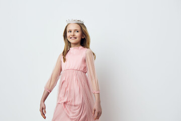 Beautiful young girl in a pink dress with a floral crown, smiling confidently against a minimalist...