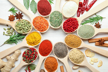 Different aromatic spices in spoons on white wooden table, flat lay