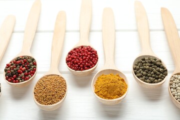 Different aromatic spices in spoons on white wooden table, closeup