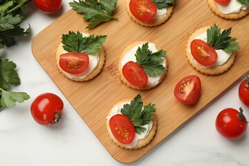 Tasty crackers with cream cheese, tomatoes and parsley on white table, flat lay