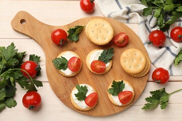 Tasty crackers with cream cheese, tomatoes and parsley on white wooden table, flat lay