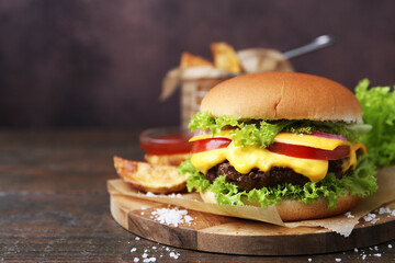 Tasty cheeseburger with potato wedges on wooden table, closeup. Space for text