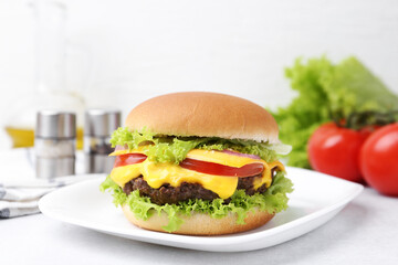 Tasty cheeseburger with lettuce and tomatoes on white table, closeup